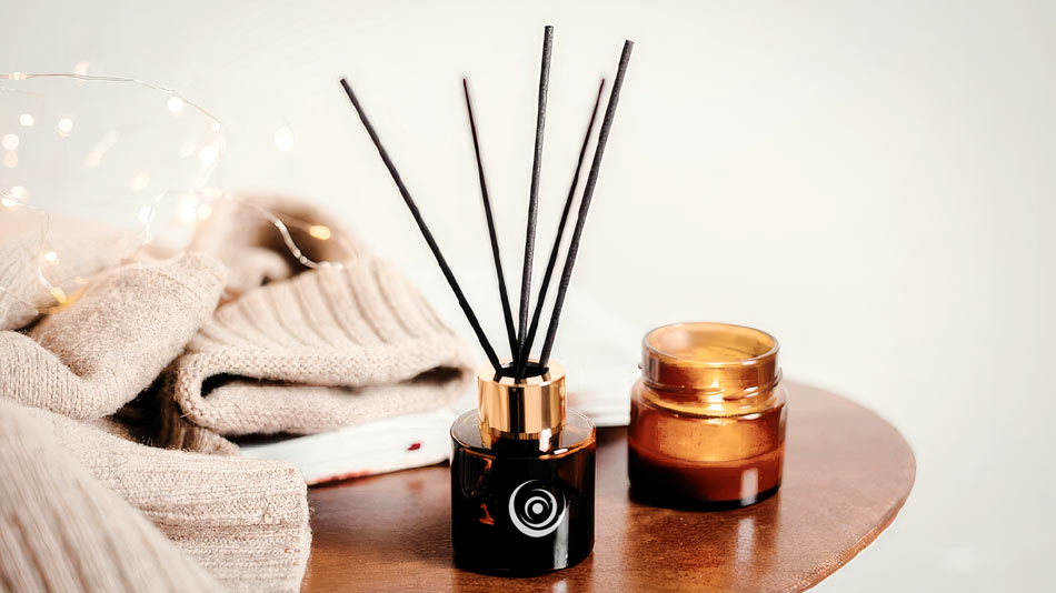 Amber glass reed diffuser with black sticks and matching scented candle in a home setting.